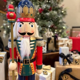 nutcracker in front of a Christmas tree full of presents